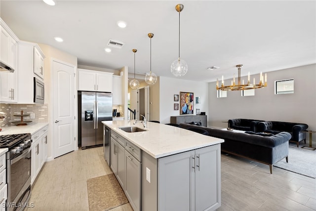 kitchen with white cabinetry, backsplash, pendant lighting, stainless steel appliances, and a center island with sink