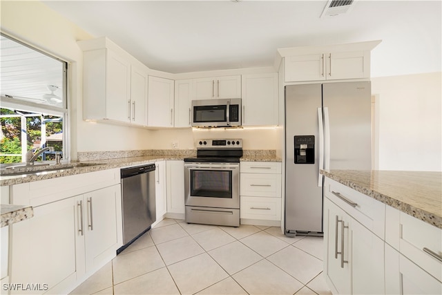 kitchen with light tile patterned flooring, stainless steel appliances, white cabinetry, light stone countertops, and sink