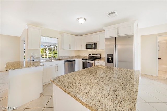 kitchen with stainless steel appliances, white cabinetry, light stone counters, and a center island