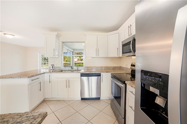 kitchen with stainless steel appliances, light tile patterned flooring, white cabinetry, and light stone counters