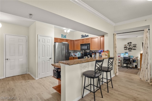 kitchen featuring ornamental molding, black appliances, light hardwood / wood-style floors, a kitchen bar, and kitchen peninsula