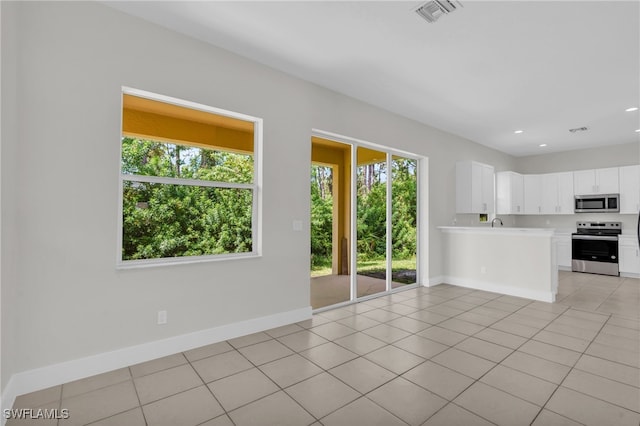 kitchen featuring white cabinets, kitchen peninsula, light tile patterned floors, and stainless steel appliances