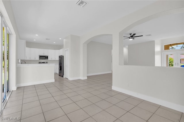 interior space featuring light tile patterned flooring, white cabinets, kitchen peninsula, appliances with stainless steel finishes, and ceiling fan