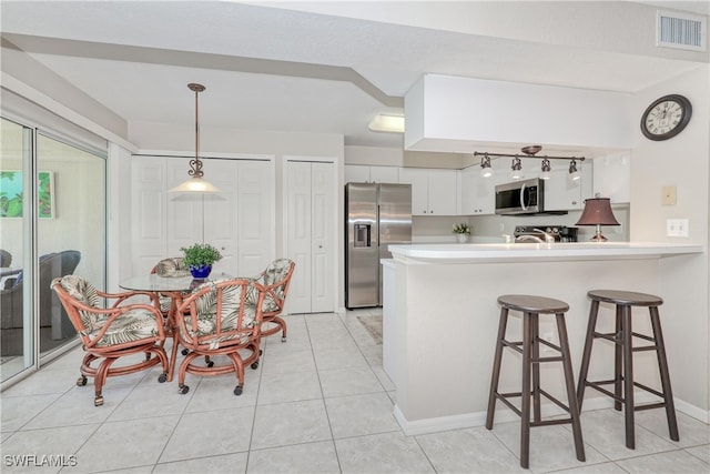 kitchen with pendant lighting, white cabinets, appliances with stainless steel finishes, a kitchen bar, and kitchen peninsula