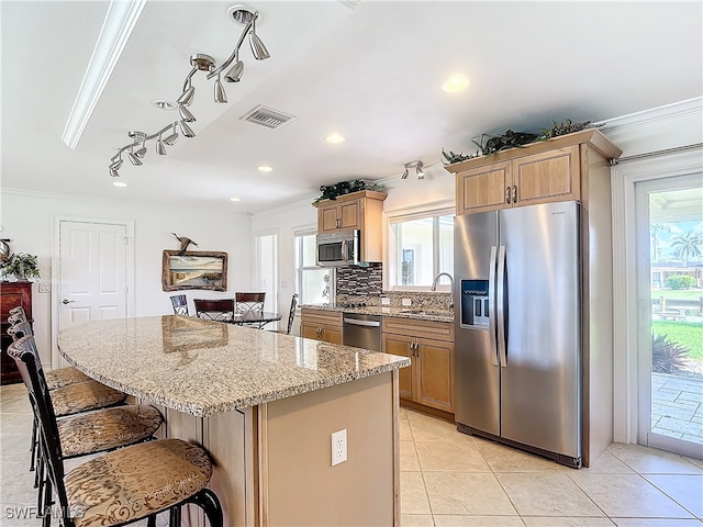 kitchen featuring crown molding, a center island, stainless steel appliances, and light stone counters