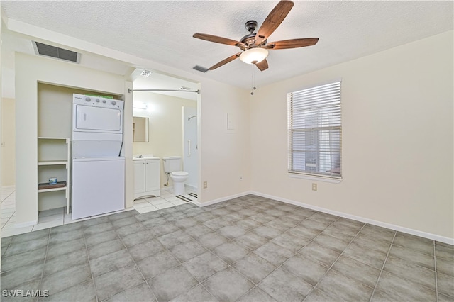 unfurnished bedroom with a textured ceiling, stacked washer and clothes dryer, ensuite bath, and ceiling fan