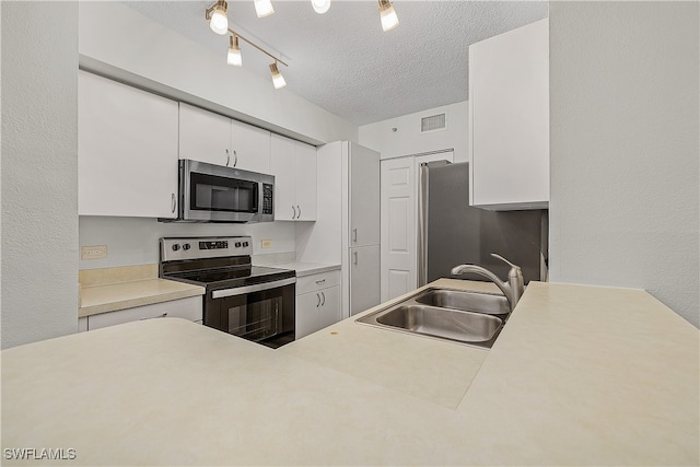 kitchen featuring sink, white cabinetry, stainless steel appliances, track lighting, and a textured ceiling