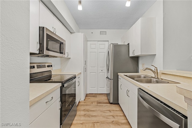 kitchen featuring sink, white cabinetry, light hardwood / wood-style flooring, a textured ceiling, and stainless steel appliances