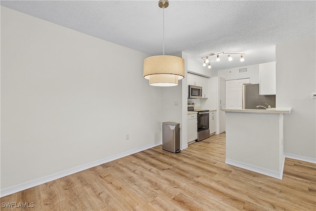 kitchen featuring pendant lighting, stainless steel appliances, a textured ceiling, white cabinets, and light wood-type flooring