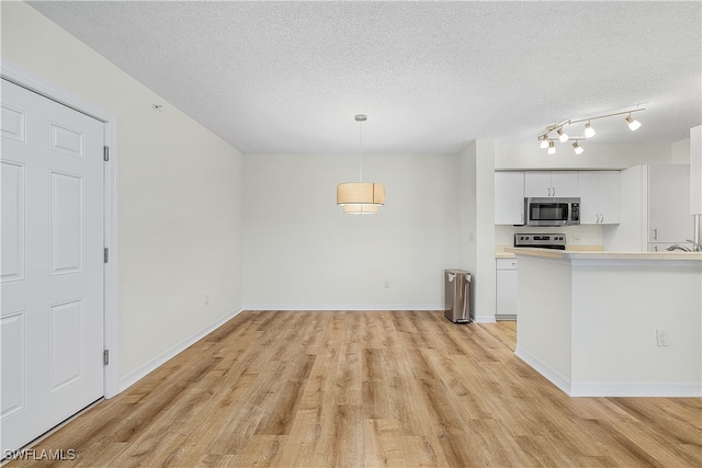 kitchen with white cabinetry, stainless steel appliances, hanging light fixtures, and light wood-type flooring