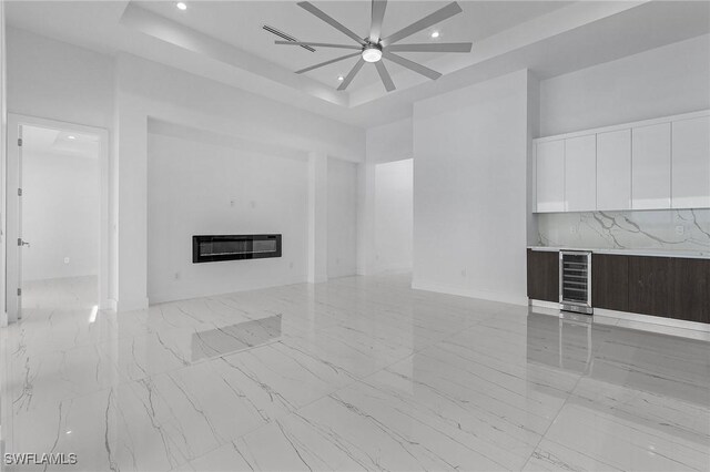 unfurnished living room with ceiling fan, heating unit, and a tray ceiling