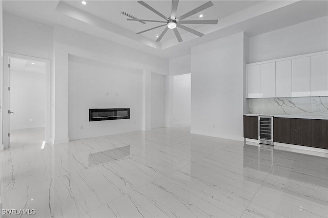 unfurnished living room featuring a raised ceiling, wine cooler, a ceiling fan, and a towering ceiling