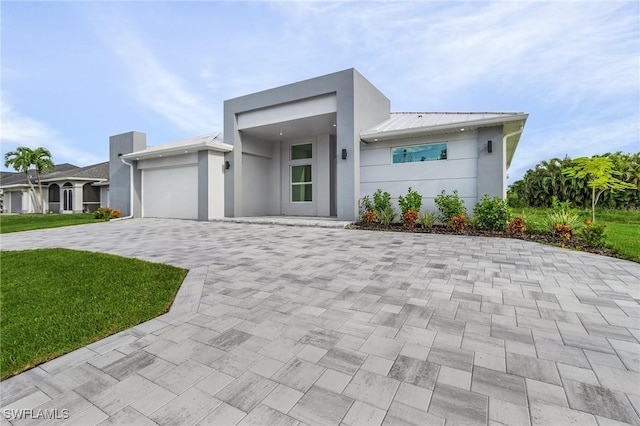 contemporary home featuring decorative driveway, a garage, a front yard, and stucco siding