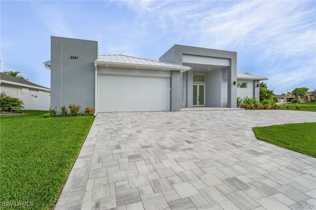 view of front of house with a front yard, a standing seam roof, french doors, decorative driveway, and metal roof