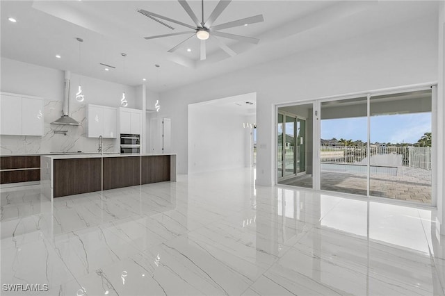 kitchen with modern cabinets, a sink, open floor plan, a high ceiling, and wall chimney range hood