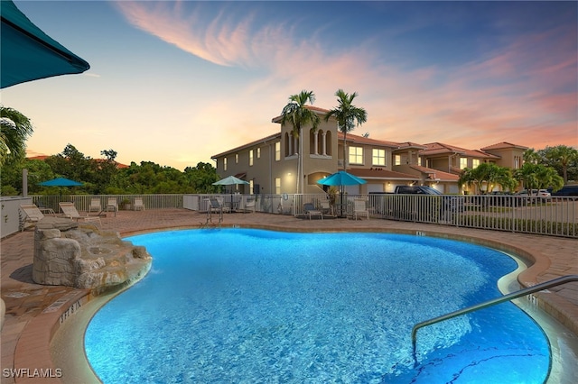 pool at dusk featuring a community pool, fence, and a patio