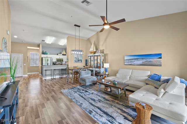 living area with ceiling fan, high vaulted ceiling, visible vents, baseboards, and light wood-style floors