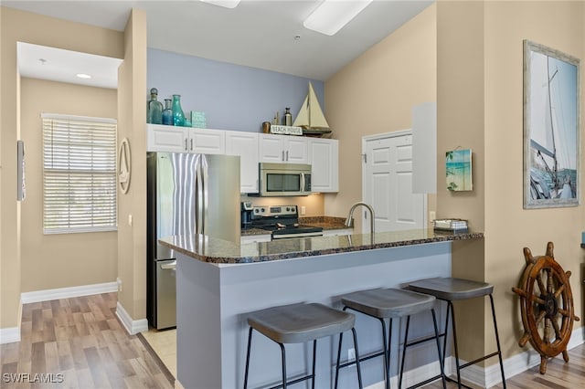 kitchen with dark stone counters, white cabinets, light wood-type flooring, appliances with stainless steel finishes, and kitchen peninsula