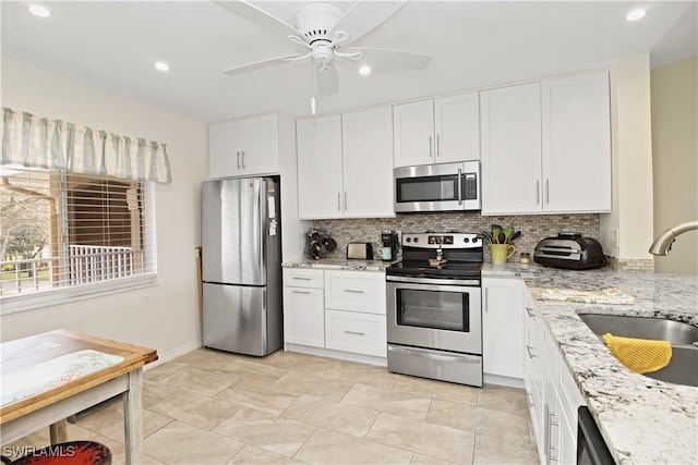 kitchen featuring ceiling fan, white cabinets, stainless steel appliances, light stone countertops, and decorative backsplash