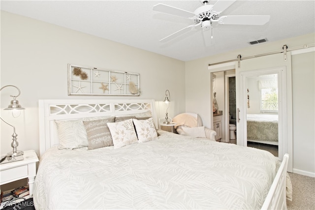 bedroom with a barn door, carpet, connected bathroom, and ceiling fan