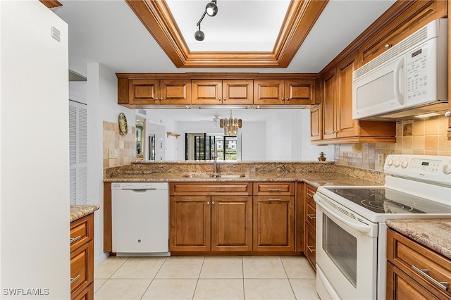 kitchen with white appliances, a tray ceiling, sink, and light stone counters