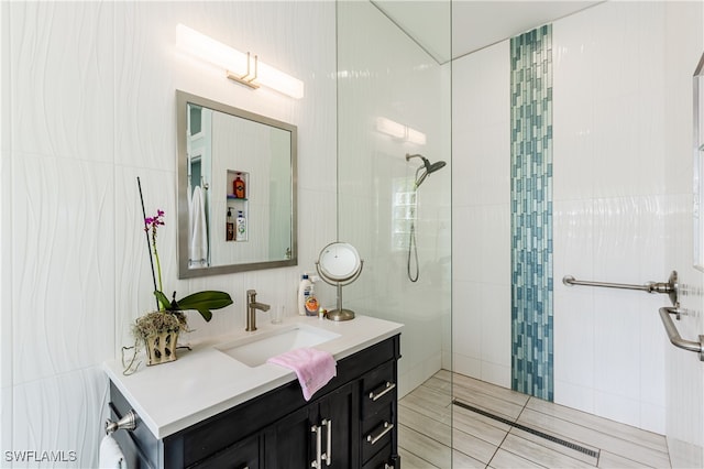 bathroom with a tile shower, vanity, and tile walls