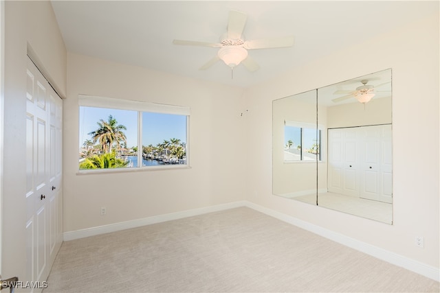 unfurnished bedroom featuring carpet, ceiling fan, a water view, and a closet