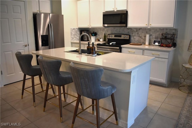 kitchen with a kitchen breakfast bar, light tile patterned floors, decorative backsplash, a sink, and stainless steel appliances