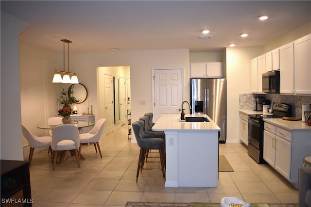 kitchen featuring pendant lighting, a kitchen island with sink, white cabinetry, backsplash, and appliances with stainless steel finishes