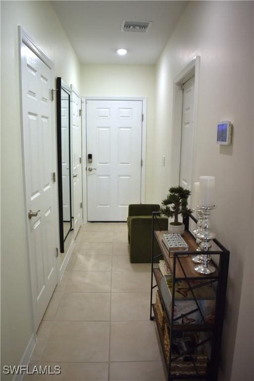 hallway with light tile patterned floors, visible vents, and baseboards