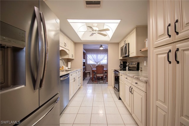 kitchen featuring ceiling fan, a skylight, sink, light tile patterned floors, and appliances with stainless steel finishes