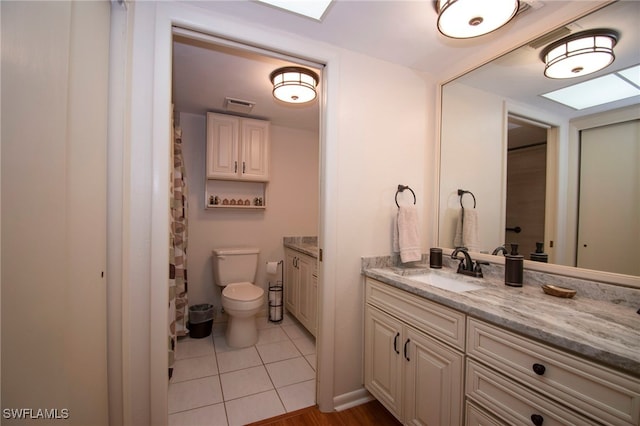 bathroom with tile patterned flooring, vanity, toilet, and a skylight