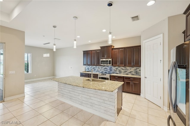 kitchen with light stone counters, pendant lighting, sink, a kitchen island with sink, and appliances with stainless steel finishes