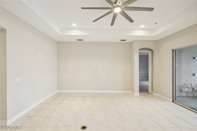 tiled empty room with ceiling fan and a tray ceiling