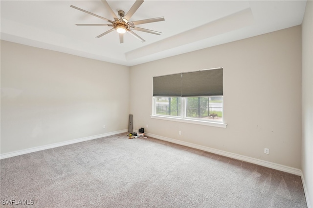 empty room with ceiling fan, carpet, and a raised ceiling