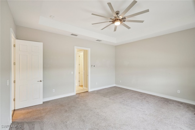 carpeted spare room featuring ceiling fan and a raised ceiling