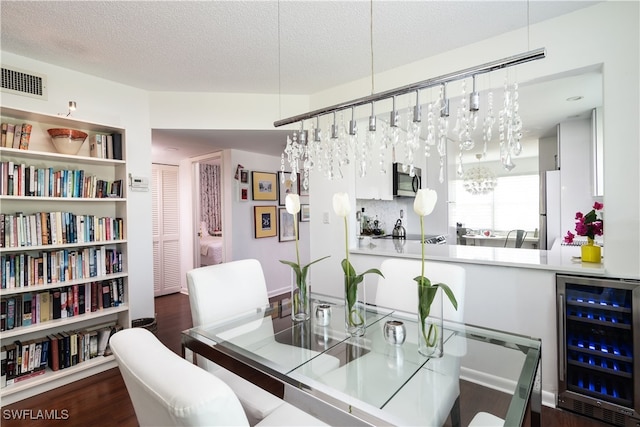 dining area with a textured ceiling, dark wood finished floors, visible vents, a chandelier, and beverage cooler