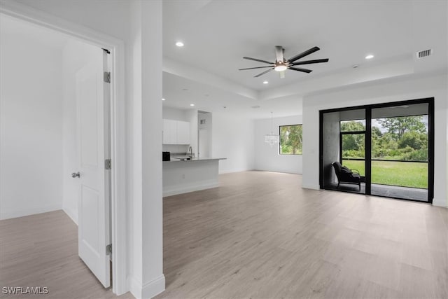 unfurnished living room with light wood-type flooring, ceiling fan, and a raised ceiling