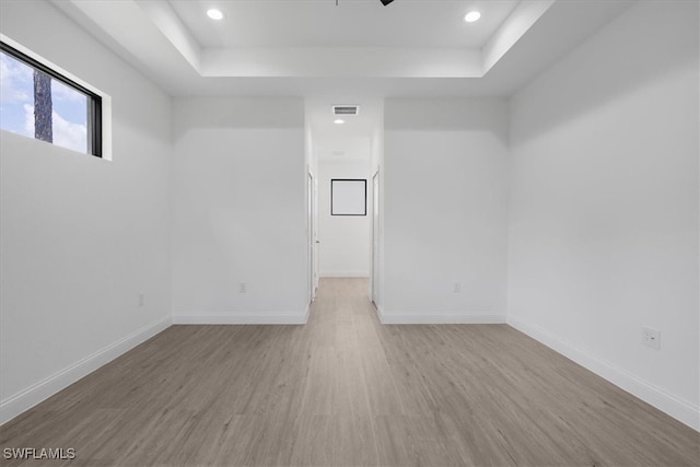 empty room with light wood-type flooring and a tray ceiling