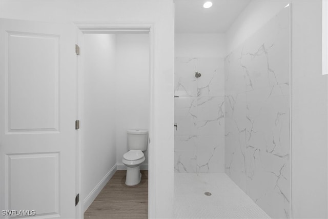 bathroom featuring wood-type flooring, tiled shower, and toilet