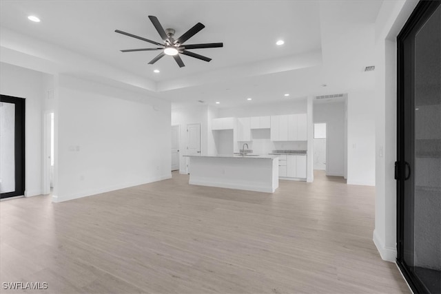 unfurnished living room with ceiling fan, light hardwood / wood-style flooring, sink, and a tray ceiling