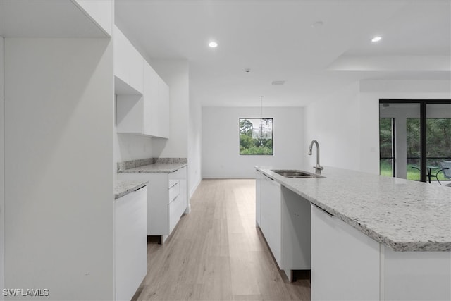 kitchen with light hardwood / wood-style flooring, white cabinets, a center island with sink, and sink