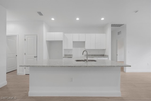 kitchen with white cabinets, light stone countertops, sink, a kitchen island with sink, and light wood-type flooring