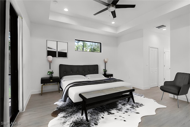 bedroom featuring ceiling fan, a tray ceiling, and light hardwood / wood-style floors