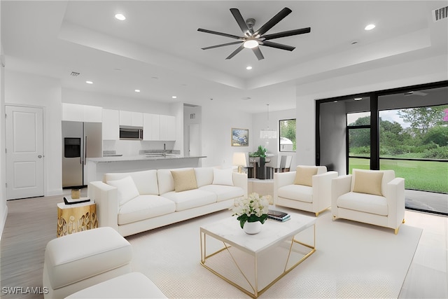 living room with a raised ceiling and ceiling fan