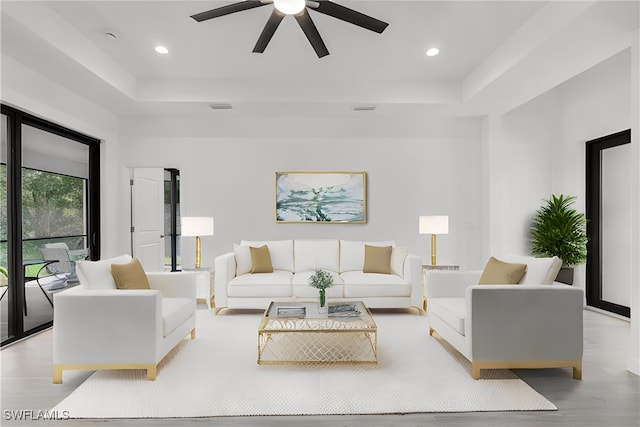 living room featuring a raised ceiling, light hardwood / wood-style floors, and ceiling fan