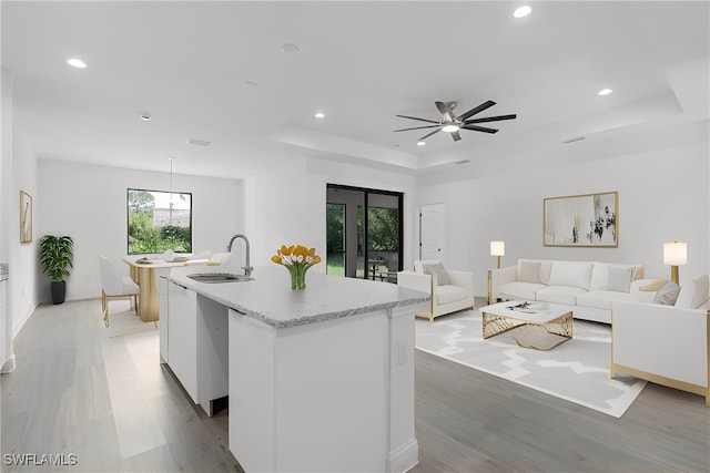 kitchen featuring white cabinetry, ceiling fan, light hardwood / wood-style flooring, a center island with sink, and sink