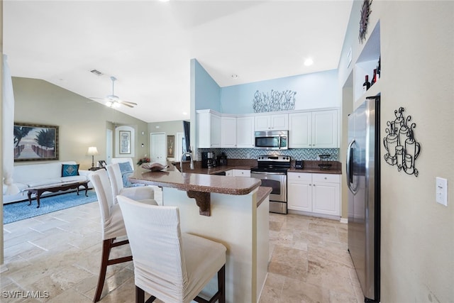 kitchen featuring a kitchen breakfast bar, a peninsula, open floor plan, dark countertops, and stainless steel appliances
