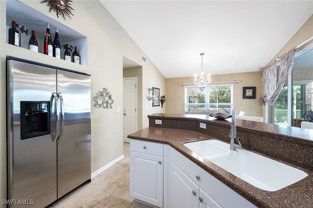 kitchen with white cabinets, vaulted ceiling, stainless steel refrigerator with ice dispenser, a sink, and a notable chandelier