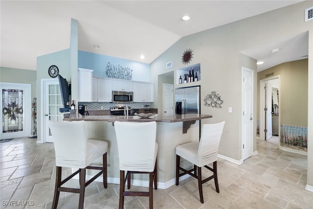 kitchen with a kitchen bar, a peninsula, appliances with stainless steel finishes, and stone tile floors